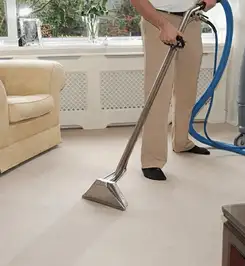 Professional carpet cleaner using a hot-water extraction wand and hose machine in a living room in Chula Vista, CA.