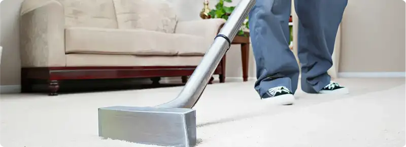 Carpet cleaning technician using a hot-water extraction wand on a light-colored carpet in a living room, Chula Vista, CA.