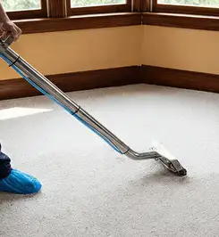 Steam carpet cleaning technician using a hot-water extraction wand on a residential carpet, wearing blue protective shoe covers Chula Vista, CA.