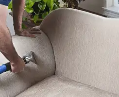 Professional upholstery cleaner deep-cleaning a fabric sofa with a handheld extraction tool and hose in Chula Vista, CA.